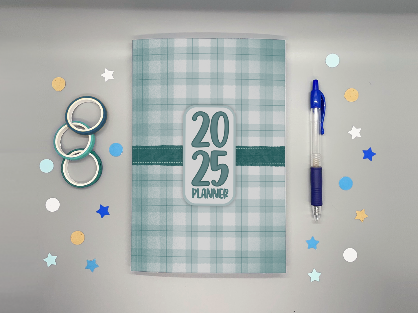 Planner with '2025' on a gray background with washi tape, confetti, and a blue pen.