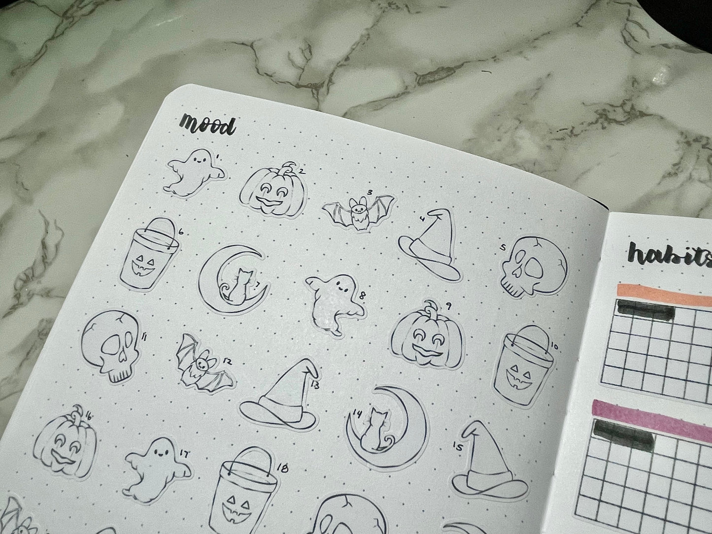 Open bullet journal with Halloween-themed stickers on a marble surface
