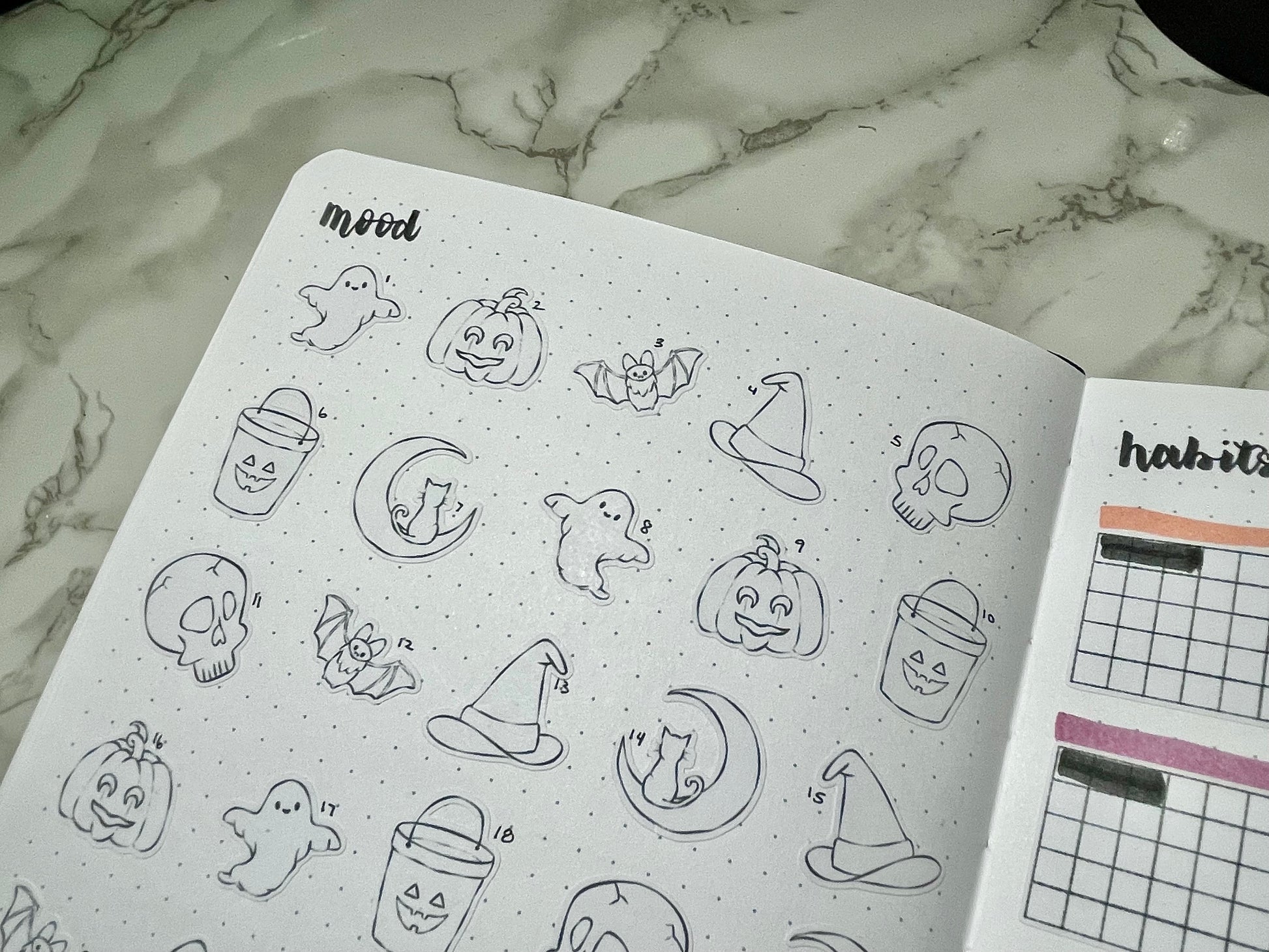Open bullet journal with Halloween-themed stickers on a marble surface