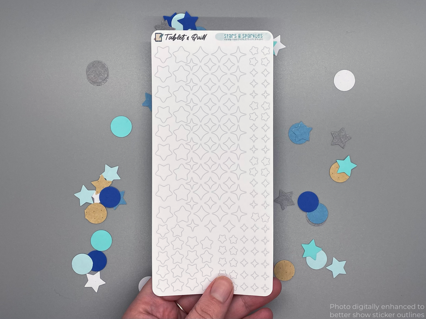 White stars and sparkles sticker sheet held by a hand on a gray background. Photo digitally enhanced to better show sticker outlines.