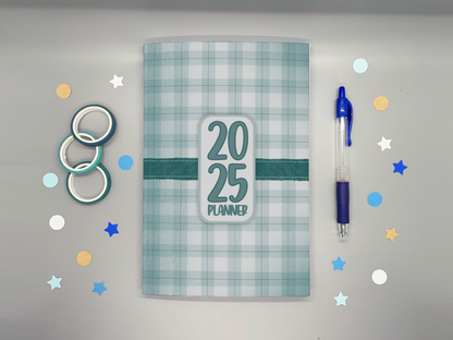 Planner with '2025' on a gray background with washi tape, confetti, and a blue pen.