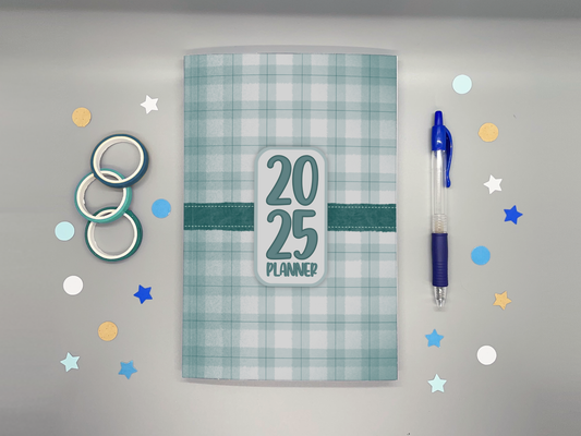 Planner with '2025' on a gray background with washi tape, confetti, and a blue pen.