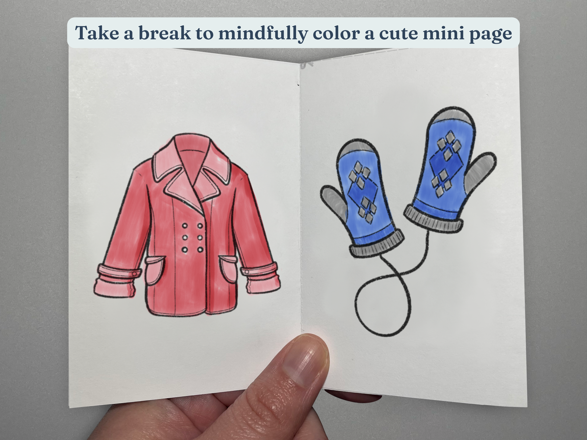 Coloring book with two items of winter clothing, one pink coat and blue mittens, held by a hand.