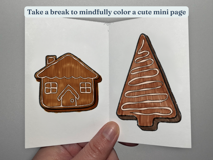 Colored in gingerbread house and tree decorations from a tiny coloring book held by a hand.
