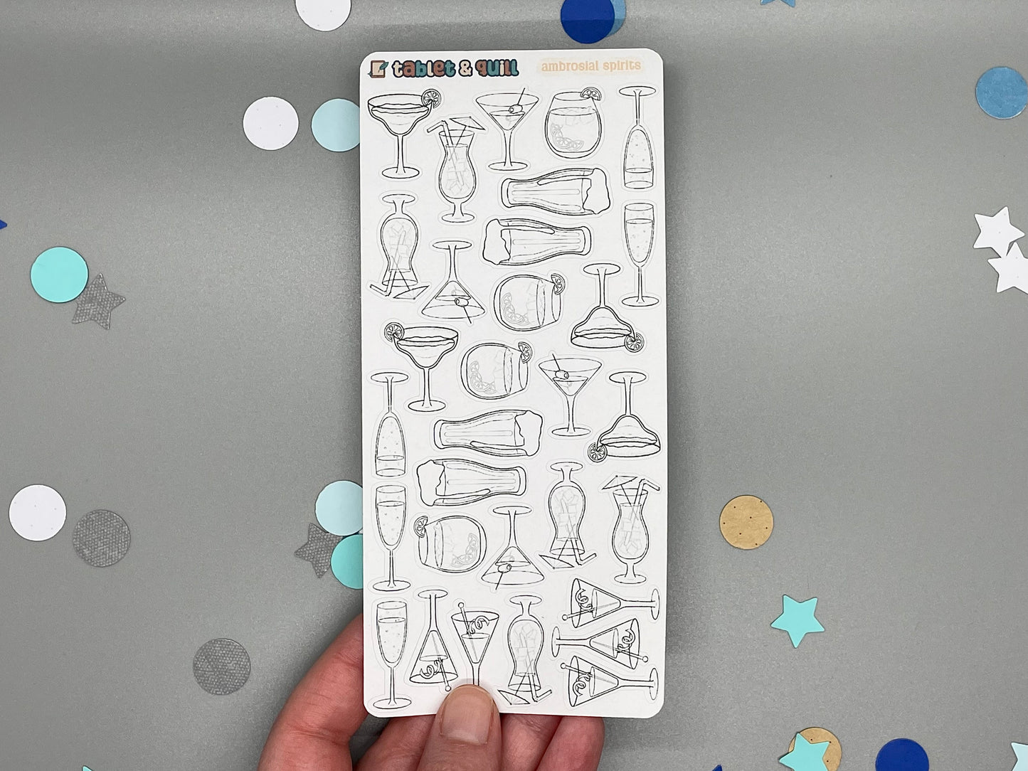 Sticker sheet of diy color drink illustrations held by a hand on a gray background with confetti.