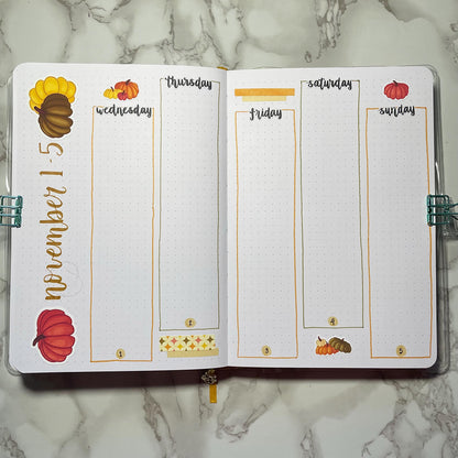 Open bullet journal showing a two page pumpkin themed weekly spread using script weekday stickers.