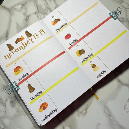 Open bullet journal showing a two page pumpkin themed weekly spread using script weekday stickers.
