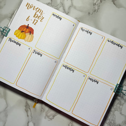 Open bullet journal showing a two page pumpkin themed weekly spread using script weekday stickers.