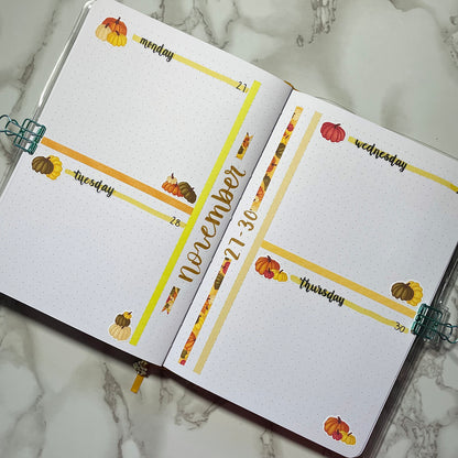 Open bullet journal showing a two page pumpkin themed weekly spread using script weekday stickers.
