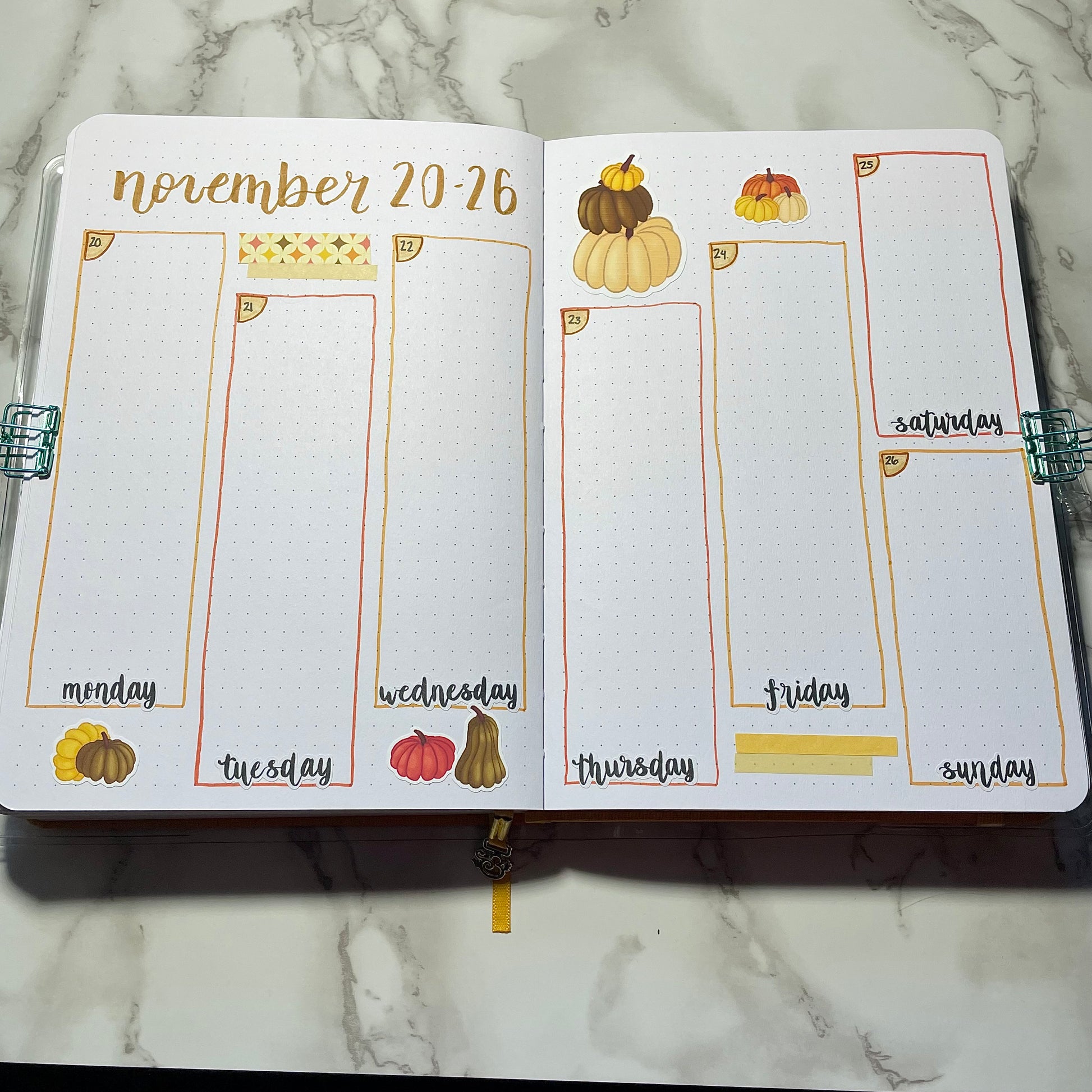 Open bullet journal showing a two page pumpkin themed weekly spread using script weekday stickers.