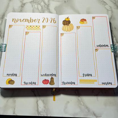 Open bullet journal showing a two page pumpkin themed weekly spread using script weekday stickers.