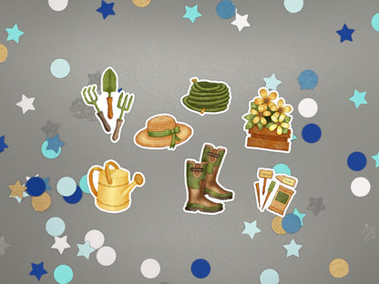 A set of garden-themed stickers arranged on a gray background with confetti. The stickers include a seed packet and markers, a coiled hose, a straw hat with a green ribbon, a flower box with yellow flowers, a watering can, a pair of green boots, and gardening tools.