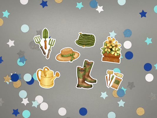 A set of garden-themed stickers arranged on a gray background with confetti. The stickers include a seed packet and markers, a coiled hose, a straw hat with a green ribbon, a flower box with yellow flowers, a watering can, a pair of green boots, and gardening tools.