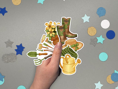 A hand holding garden themed stickers over a gray surface with confetti.