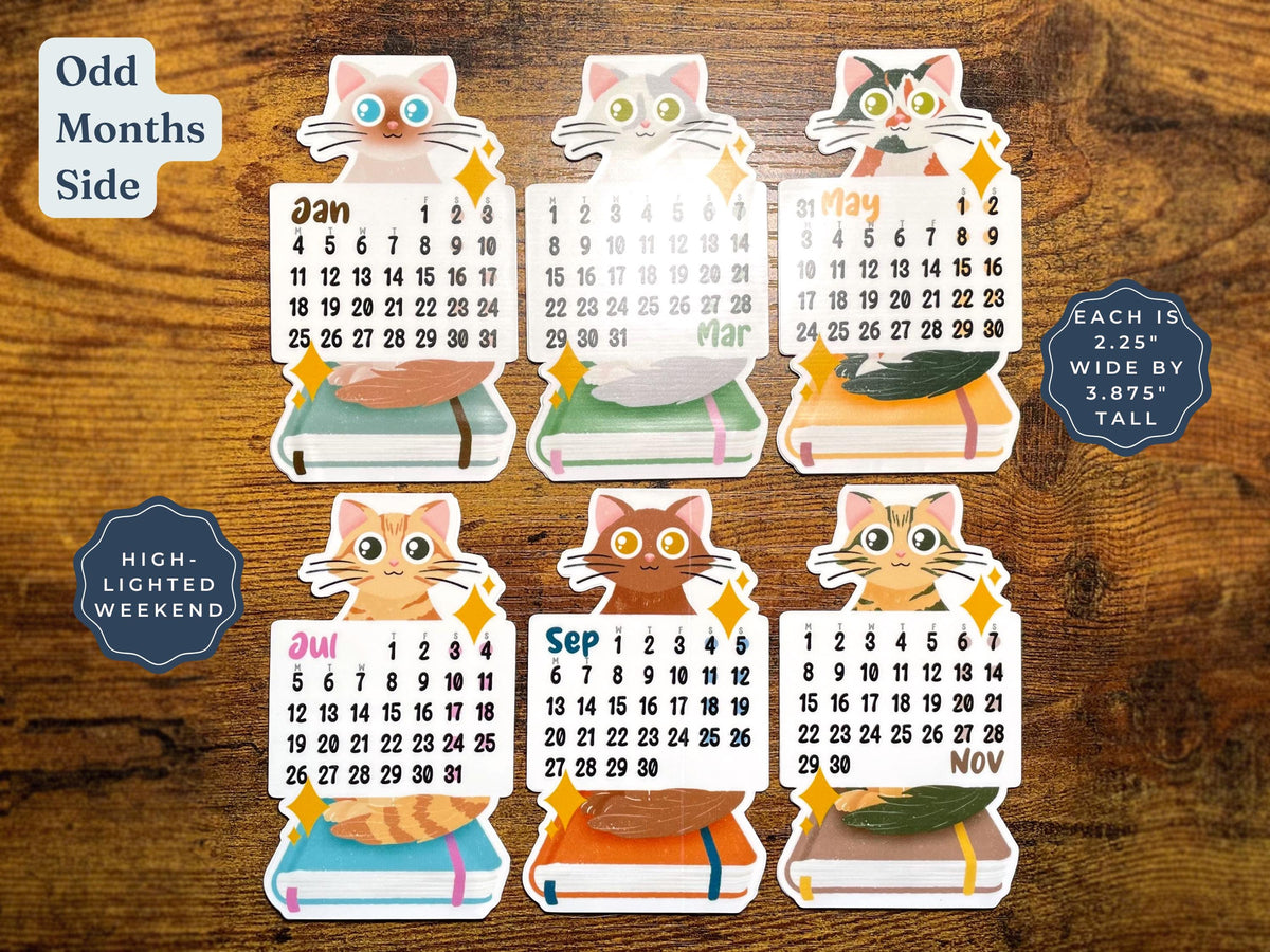 Six colorful cat-shaped monthly calendar stickers arranged on a brown wood background, with text labels including 'Odd Months Side,' 'High-Lighted Weekend,' and 'Each is 2.25" wide by 3.875".