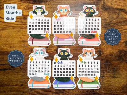 Six colorful cat-shaped monthly calendar stickers arranged on a brown wood background, with text labels including 'Even Months Side,' 'High-Lighted Weekend,' and 'Each is 2.25" wide by 3.875".