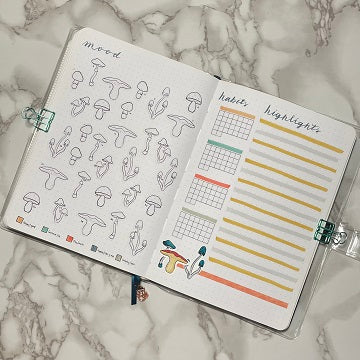 Overview image of a two page spread. The left page is labeled Mood and has 30 colorable mushroom stickers not yet colored. The bottom has a 5 color rating scale. The right page is labeled habits with 4 mini blank calendars below and next to it is labeled Highlights with 30 blank lines in alternating colors.