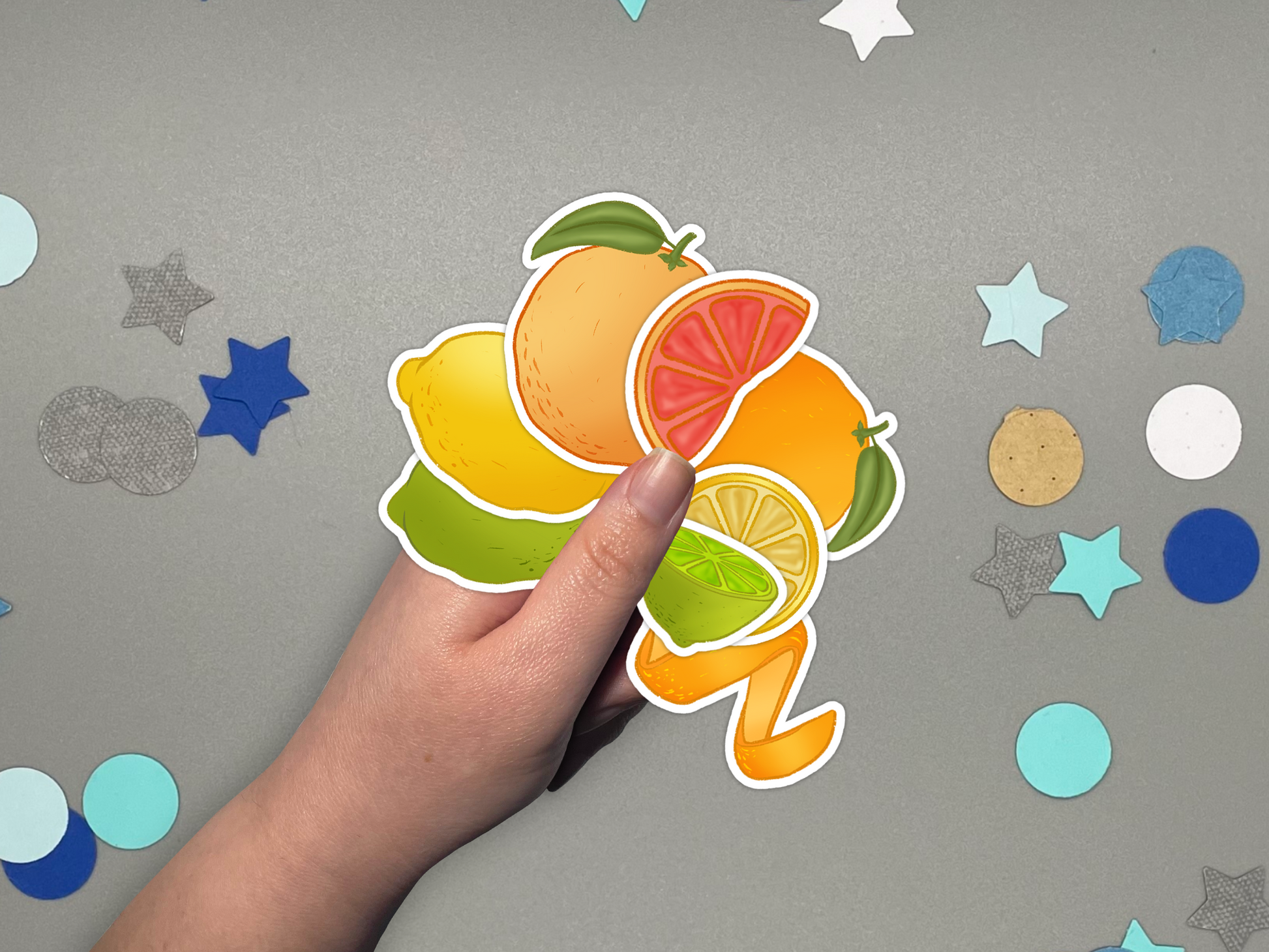 Hand holding colorful citrus themed bullet journal stickers on a gray background with decorative elements.