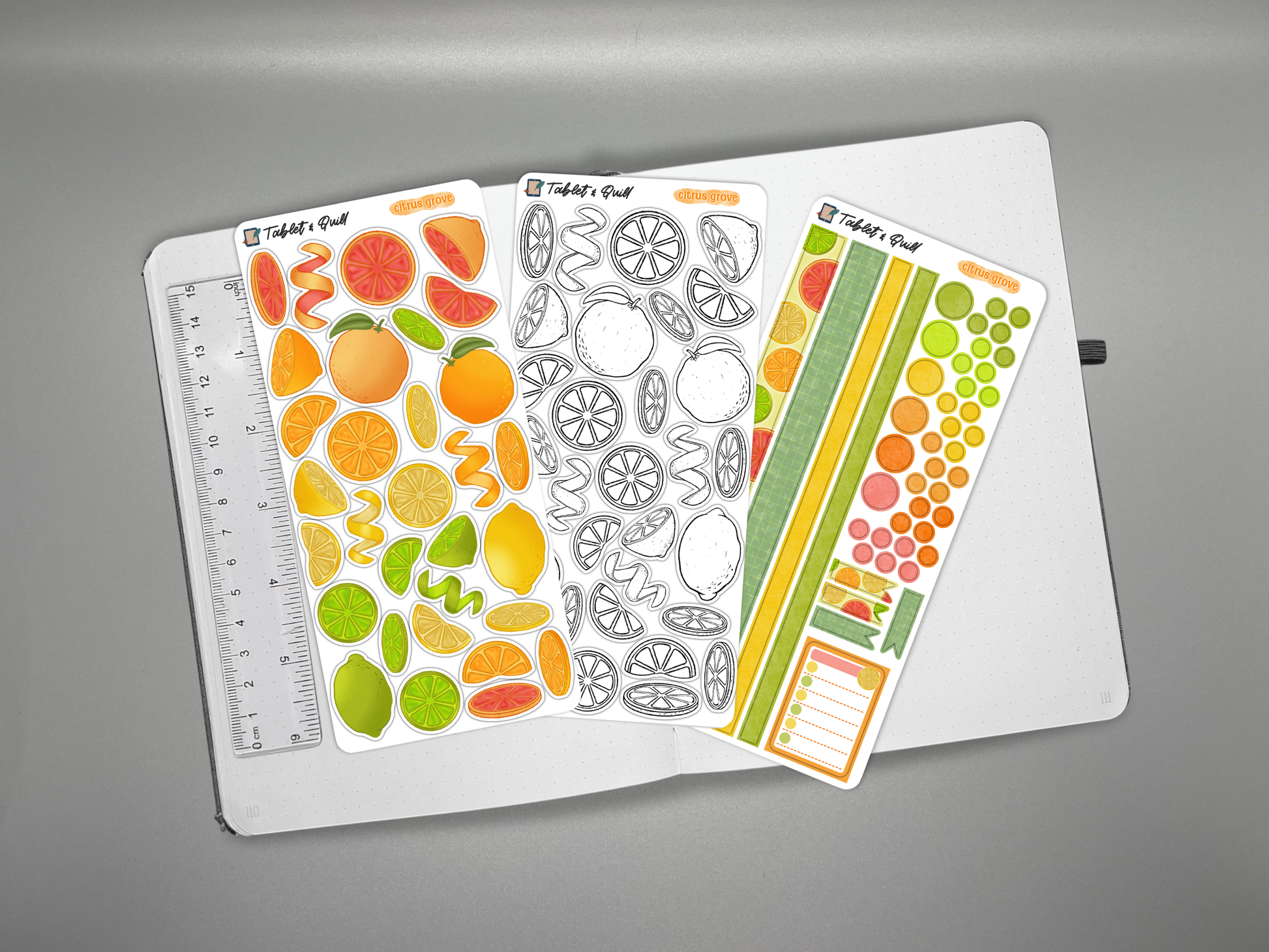 Set of colorful citrus themed bullet journal stickers on a journal with a ruler for scale over a gray background with decorative elements.
