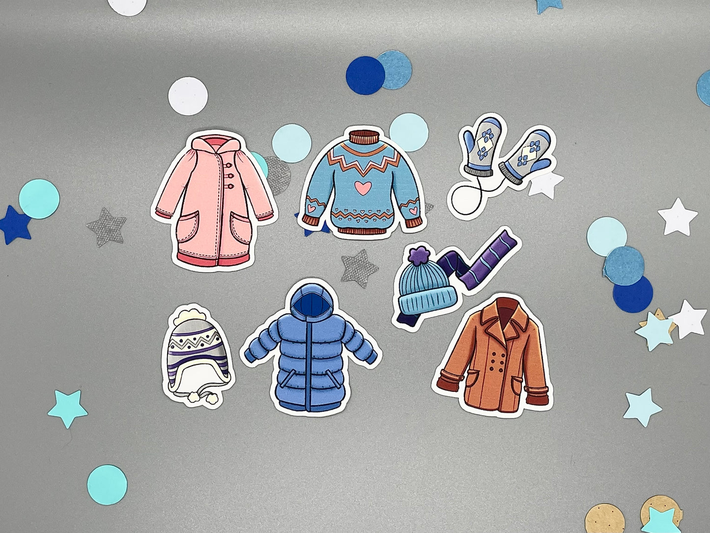Stickers of winter clothing items on a gray background with star-shaped confetti.