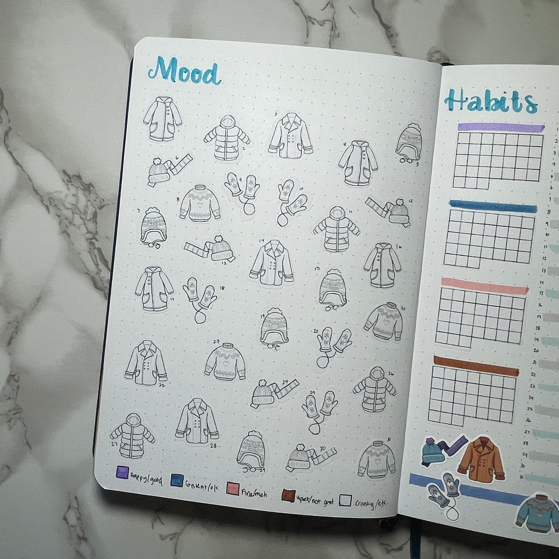 Bullet journal with mood and habits pages on a marble surface. The mood tracker is using winter clothes themed DIY color stickers.