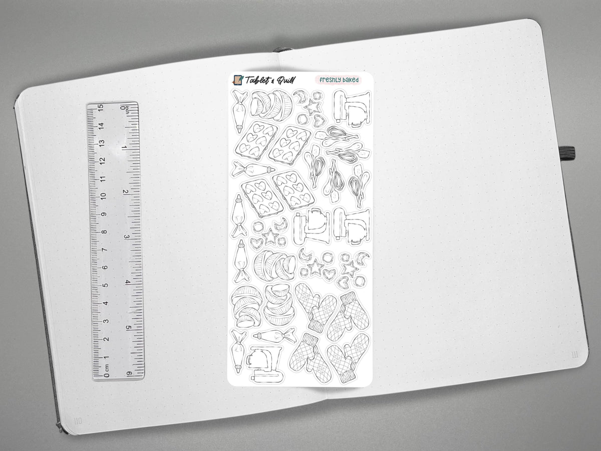 Black and white baking themed sticker sheet on an open journal with a ruler on the left for scale, all over a gray surface.
