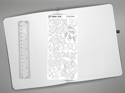 Black and white baking themed sticker sheet on an open journal with a ruler on the left for scale, all over a gray surface.