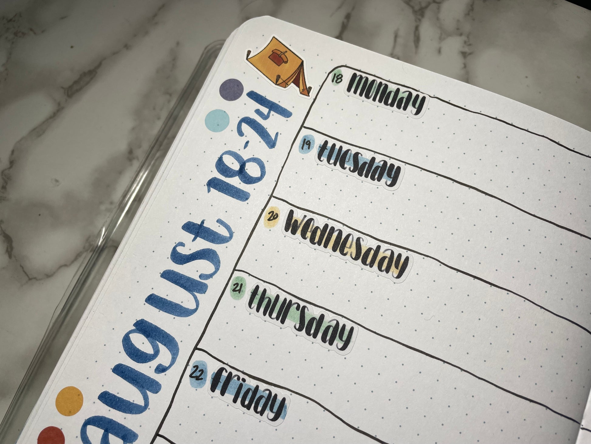 Close up of a weekly bullet journal spread using lettering weekday stickers and camping themed stickers.