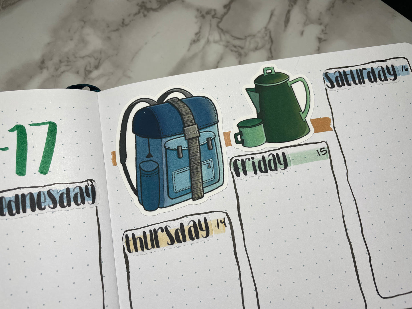 Close up of a weekly bullet journal spread decorated using camping themed stickers and hand lettered weekday stickers.