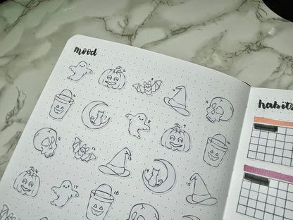 Open bullet journal with Halloween-themed stickers on a marble surface