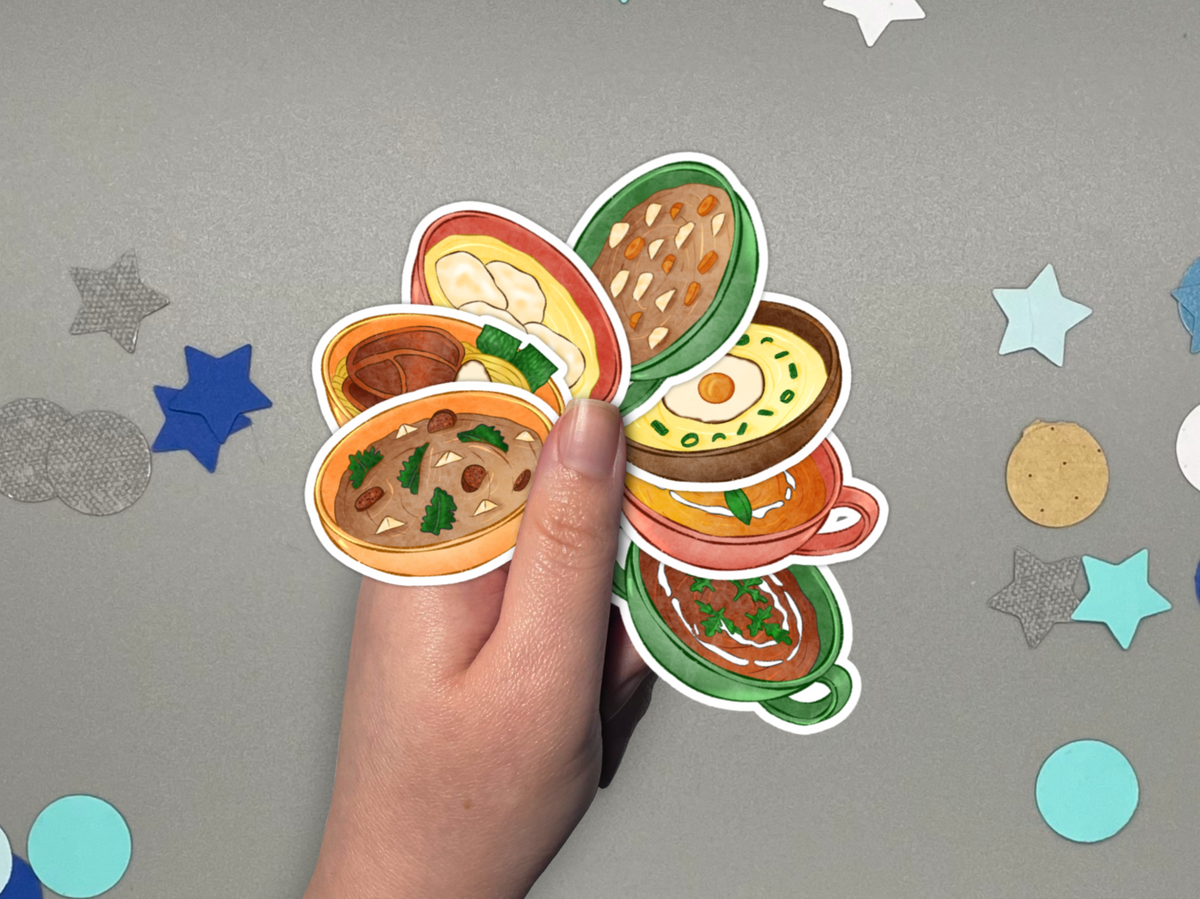 A hand holds a cluster of colorful illustrated soup stickers, shown against a gray background with scattered star and circle confetti.