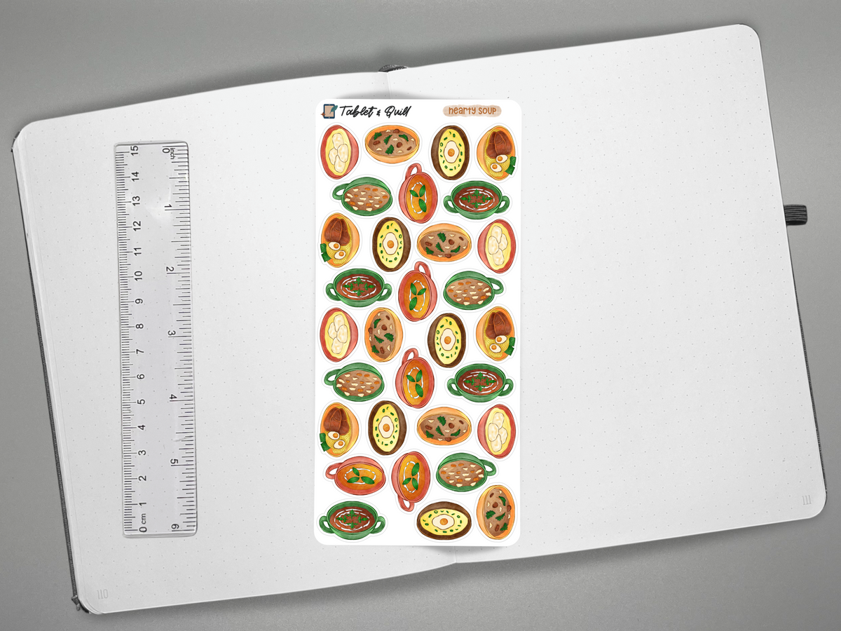 A sheet of colorful soup stickers displayed on an open white notebook next to a ruler for scale, photographed from above on a gray background.