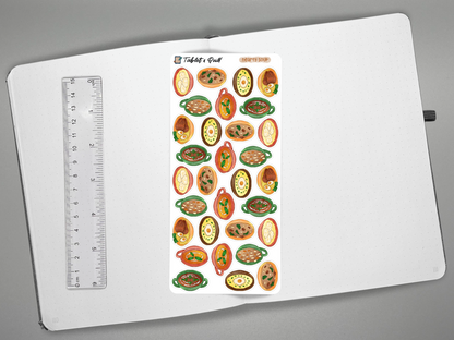A sheet of colorful soup stickers displayed on an open white notebook next to a ruler for scale, photographed from above on a gray background.