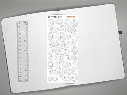An open journal photographed from above on a gray background, featuring a ruler on the left and a sheet of soup DIY color stickers.
