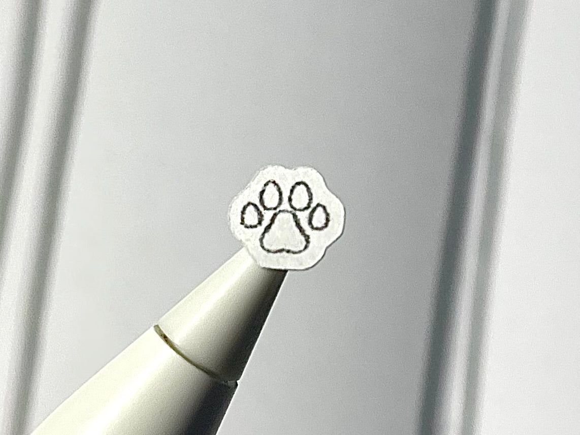 Close-up of a stylus with a paw print sticker on a blurry journal background.