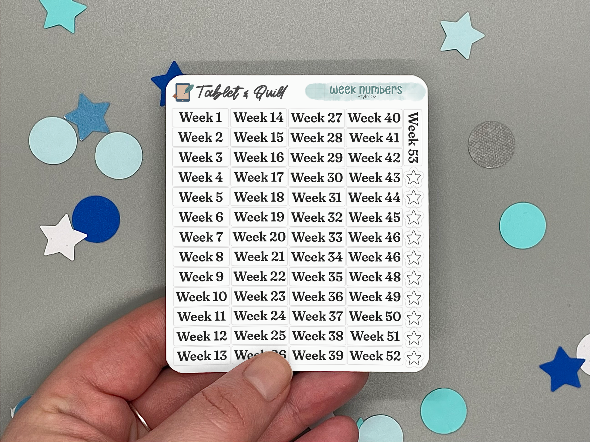 Hand holding a planner sticker sheet with week numbers on a gray background with decorative stickers.