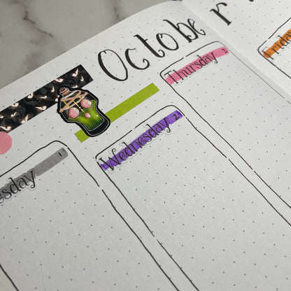 Closeup of an open bullet journal showing a two page potions themed weekly spread using serif weekday stickers.