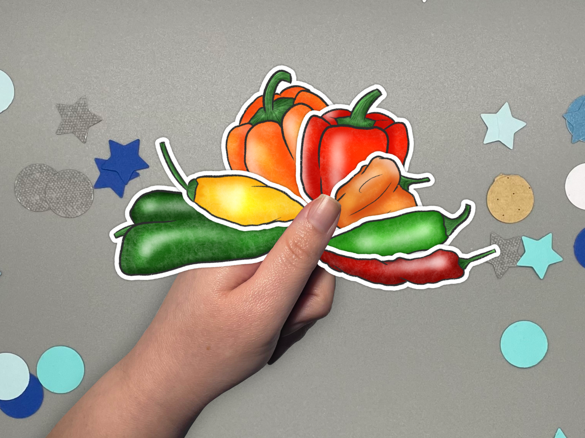 Colorful pepper sticker held by a hand against a gray background with star and circle confetti.