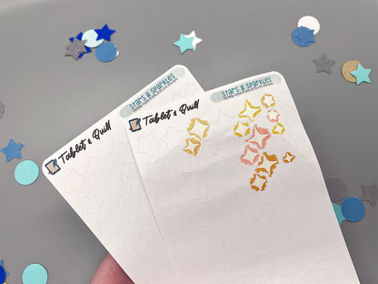 Closeup of two stars and sparkles sticker sheets on a gray background. One sticker sheet has some stars removed.