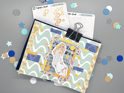 Two stars and sparkles DIY color sticker sheets on a gray background. One sheet has colored sparkles that are removed from the sheet. A small journal sits on top decorated with paper and stickers, including koi stickers colored with colored pencils and stars and sparkles colored with markers.
