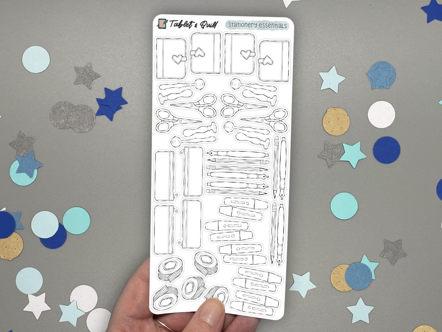 Stationery themed DIY color bullet journal stickers held by a hand and over a gray background with confetti. 