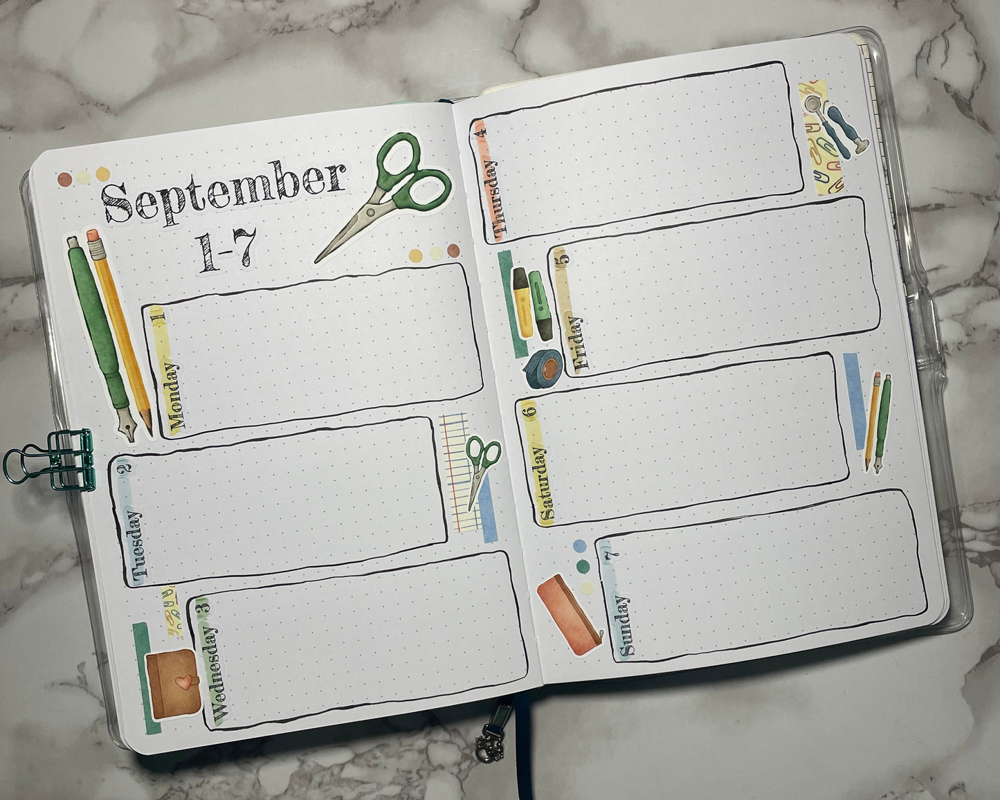 Open bullet journal weekly spread with custom header stickers and stationery themed stickers.