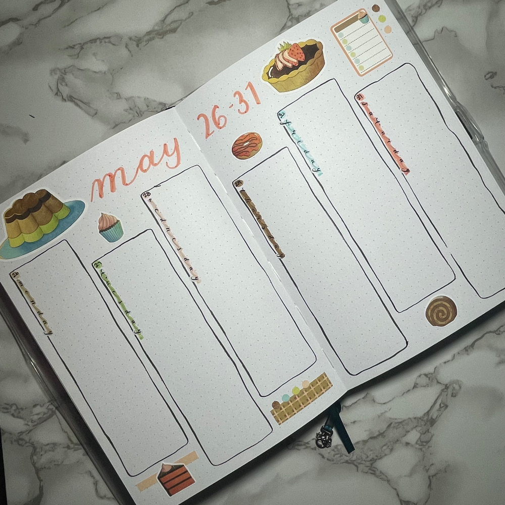 Bullet journal weekly spread with dessert themed decorative stickers on a marble surface