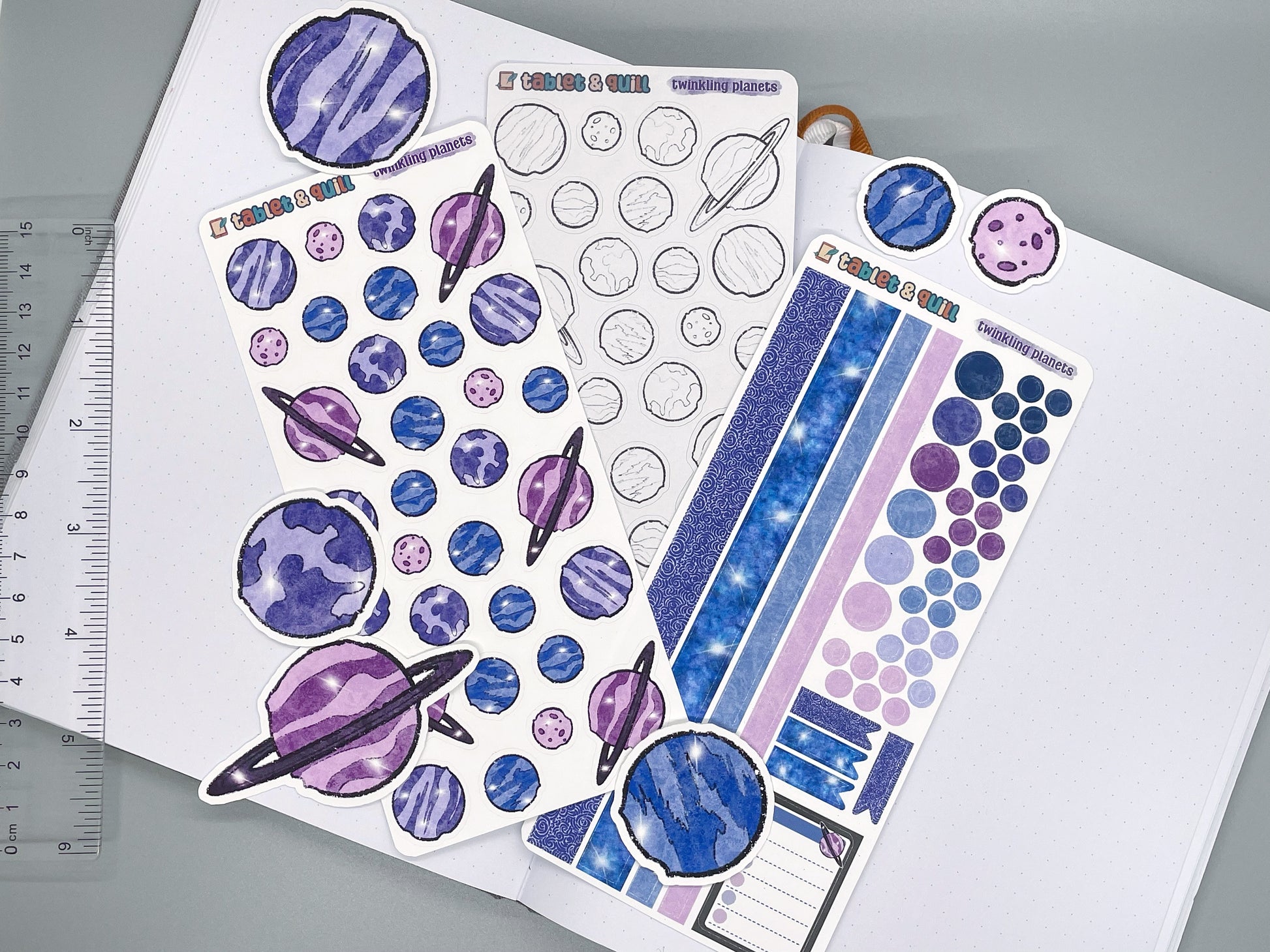 Twinkling planets sticker sheets and die cut stickers on journal with ruler on gray background.