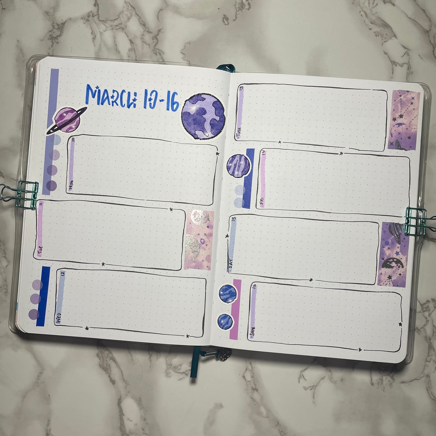 Bullet journal weekly spread with purple and blue planet stickers on a marble surface.