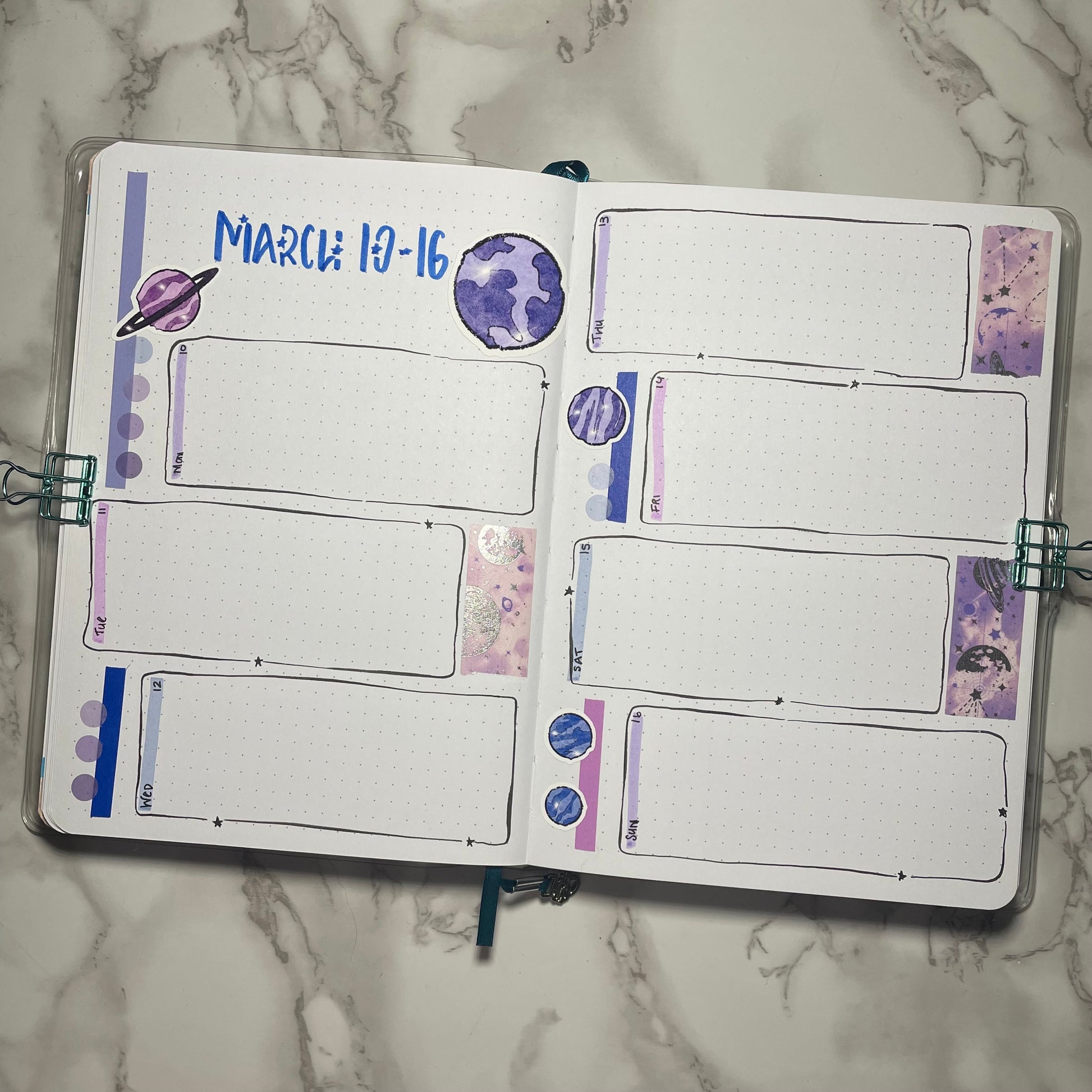 Bullet journal weekly spread with purple and blue planet stickers on a marble surface.