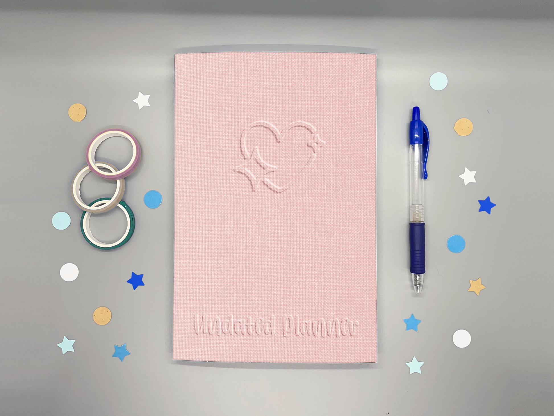 Pink planner with embossed design on a gray background with colorful stars and washi tape.