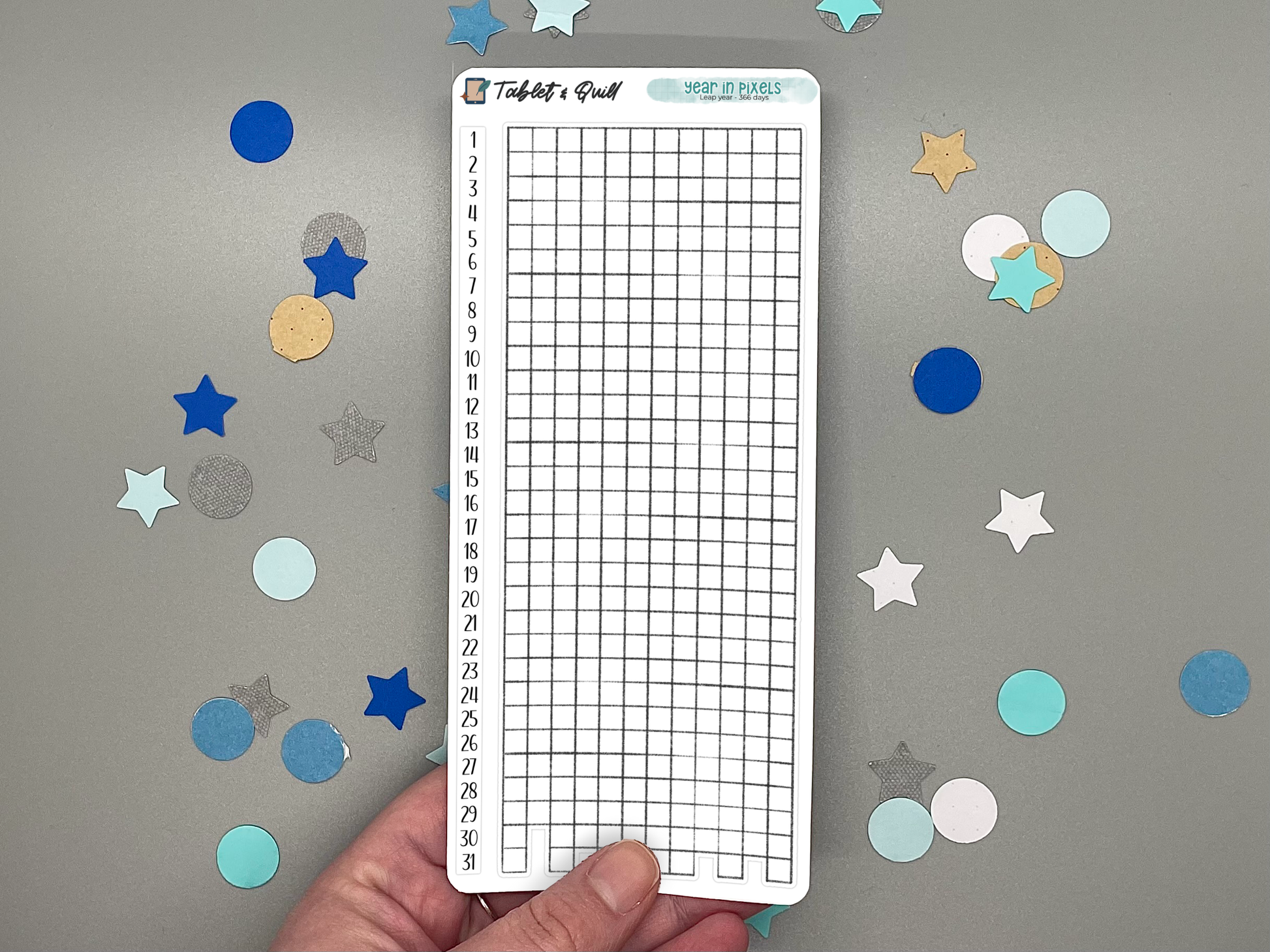 Hand holding a year in pixels with vertical number strip sticker sheet for a leap 366-day year on a gray background with colorful stars and circles.